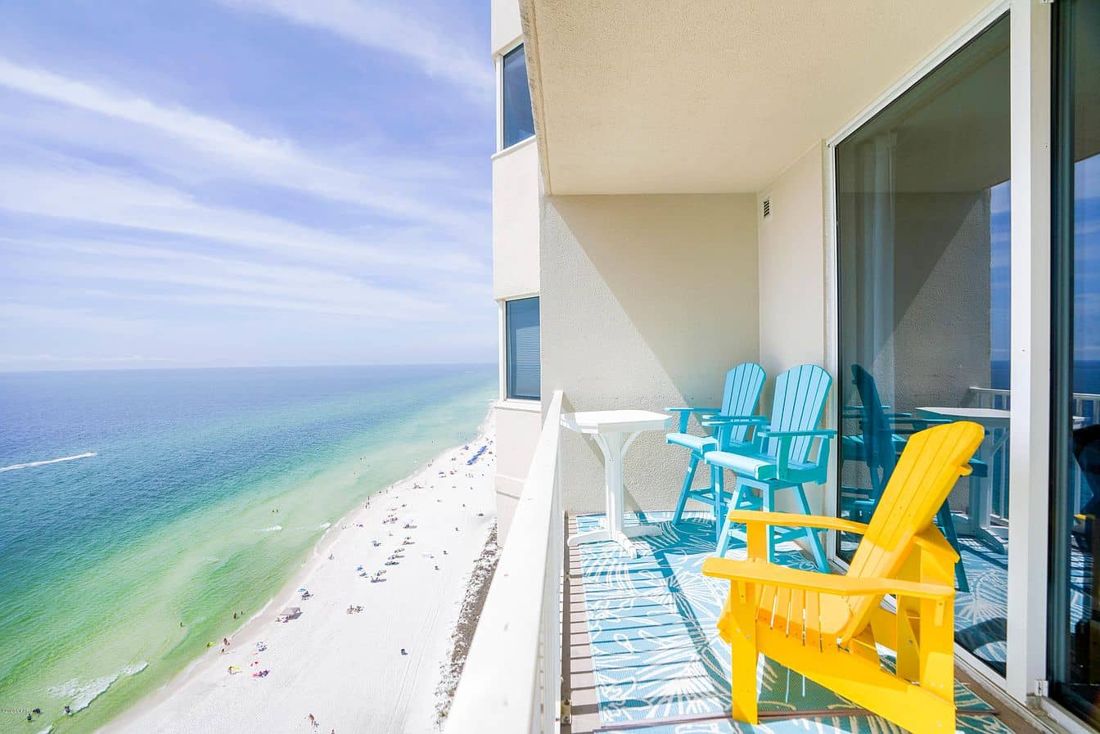 View from one of Eliseo's rental balconies: white sand beach and emerald Gulf water below, with yellow and turquoise chairs